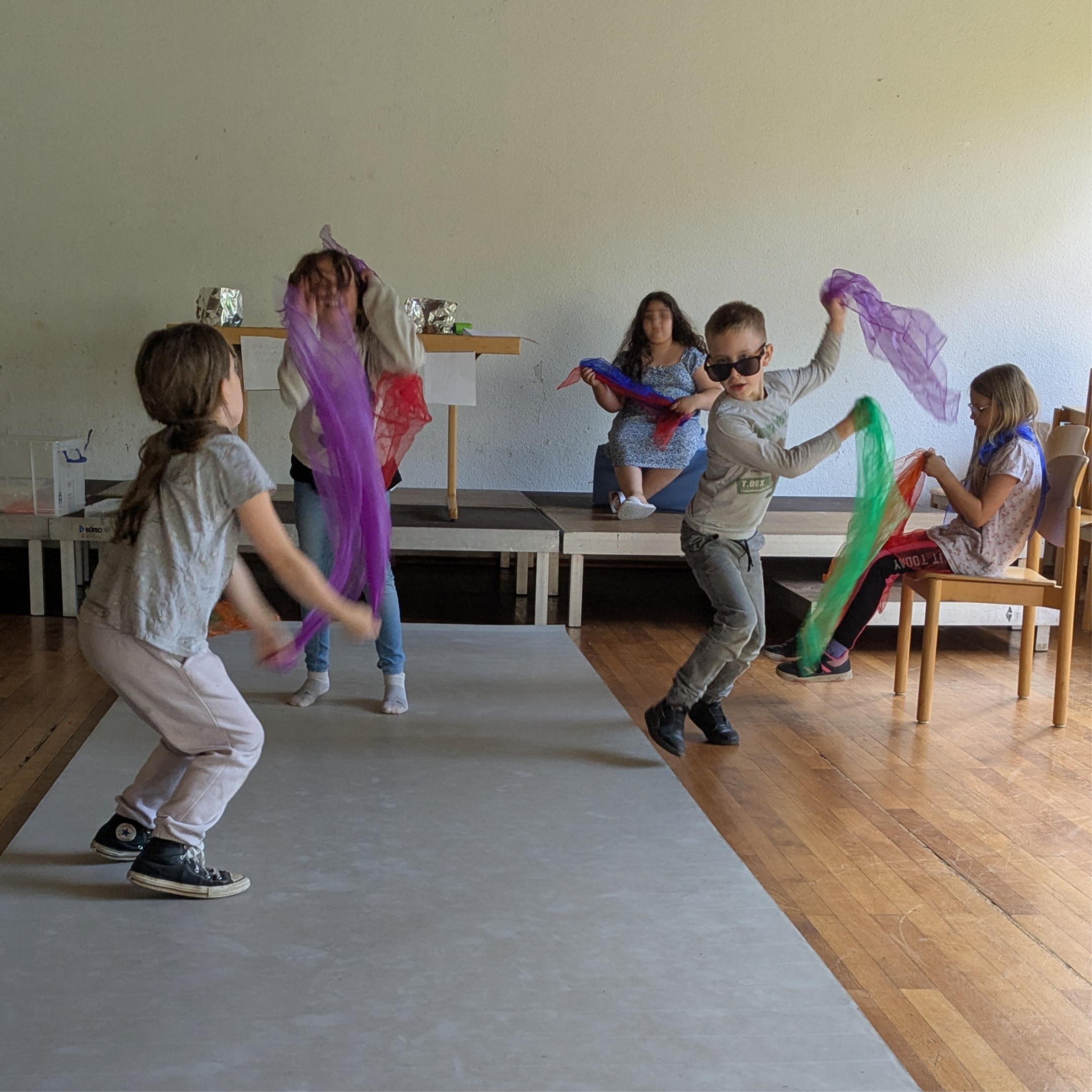 Kinder tanzen mit Tüchern über einen grauen Laufsteg.