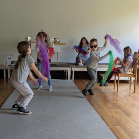 Kinder tanzen mit Tüchern über einen grauen Laufsteg.