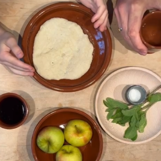 braune Teller mit Brotfladen, Äpfel, Salz und Bitterkräutern. Hände die den Teller halten und eine andere Hand, die den Becher mit Wein hält.