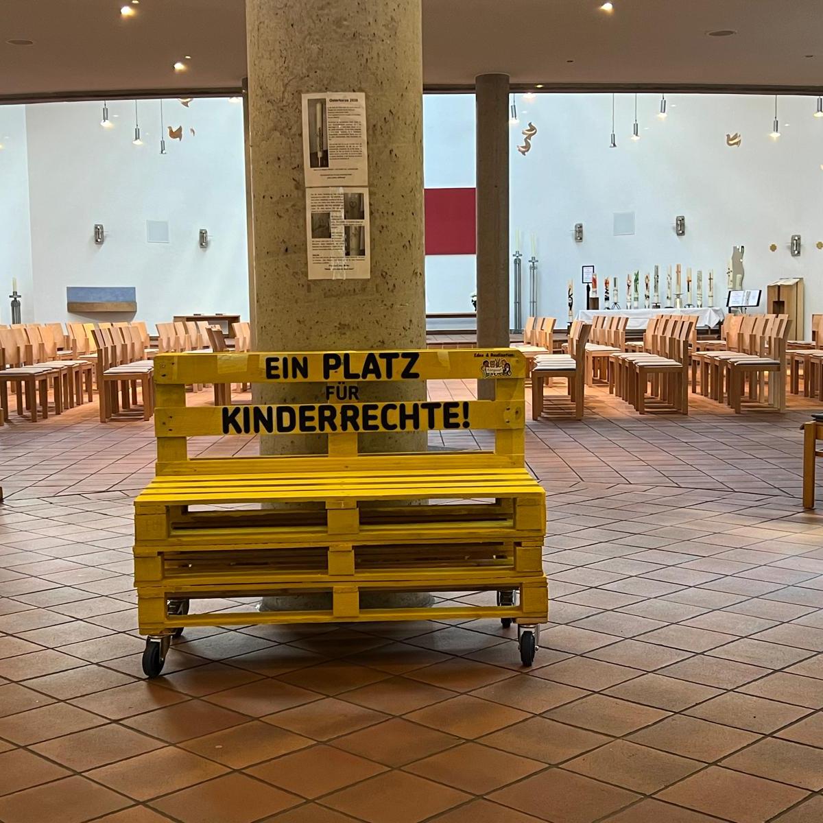 Ein gelbes Palettensofa steht vor einer grauen Säule.