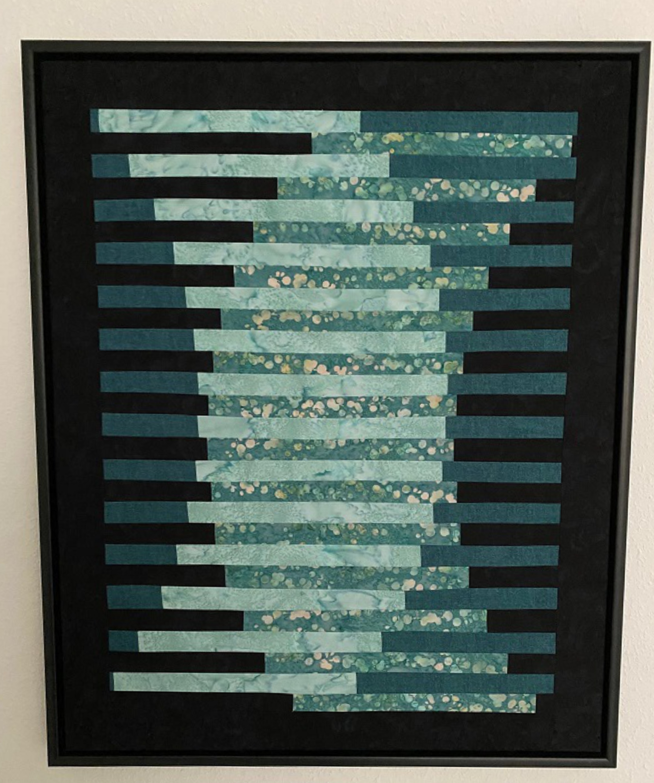 Ein gerahmtes Bild hängt an einer weißen Wand. Das Bild besteht aus vielen waagerechten Streifen in Blau- und Grüntönen. Die Streifen bilden zusammen ein abstraktes Muster.