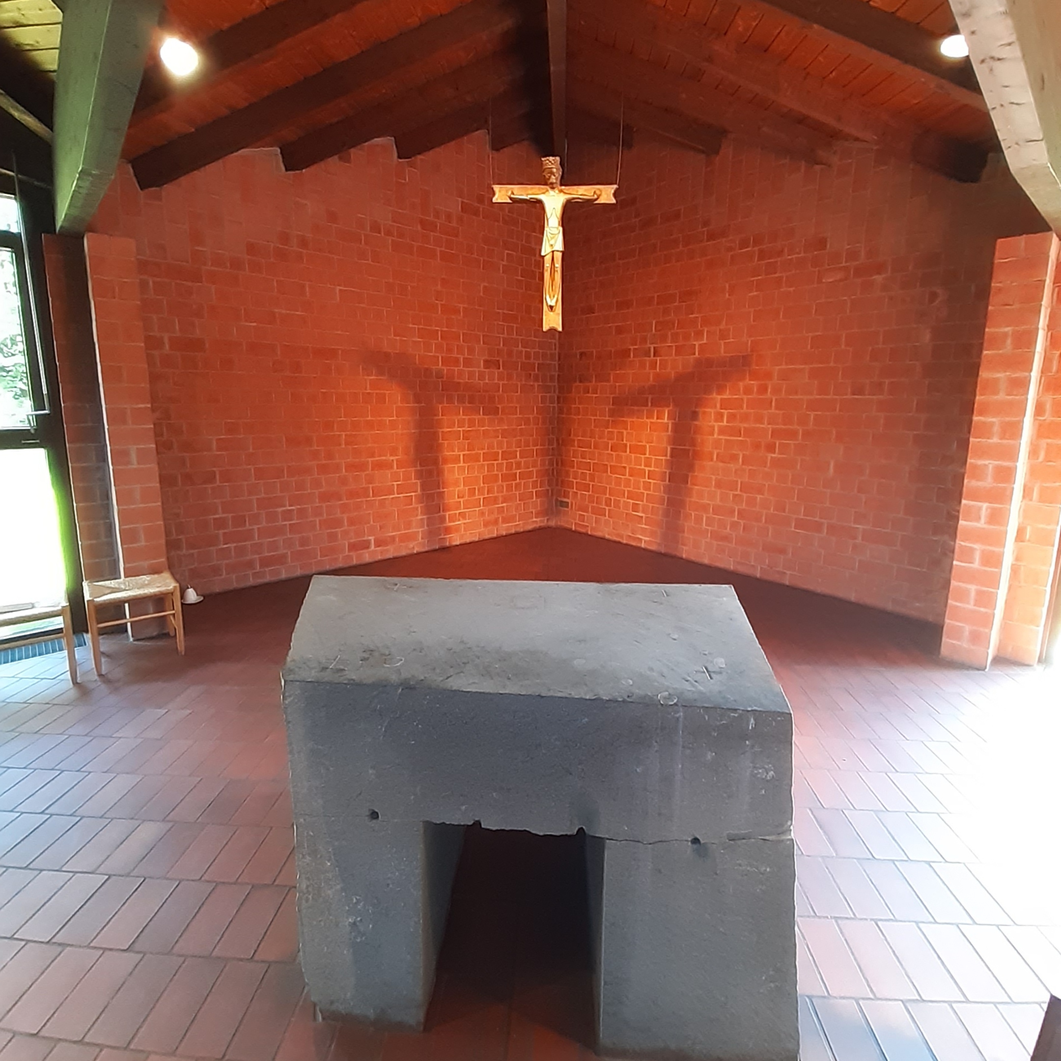 Blick über den Steinaltar zu dem einen Kreuz, das durch die Architektur und das Licht drei Kreuzschatten an der Apsiswand darstellt.