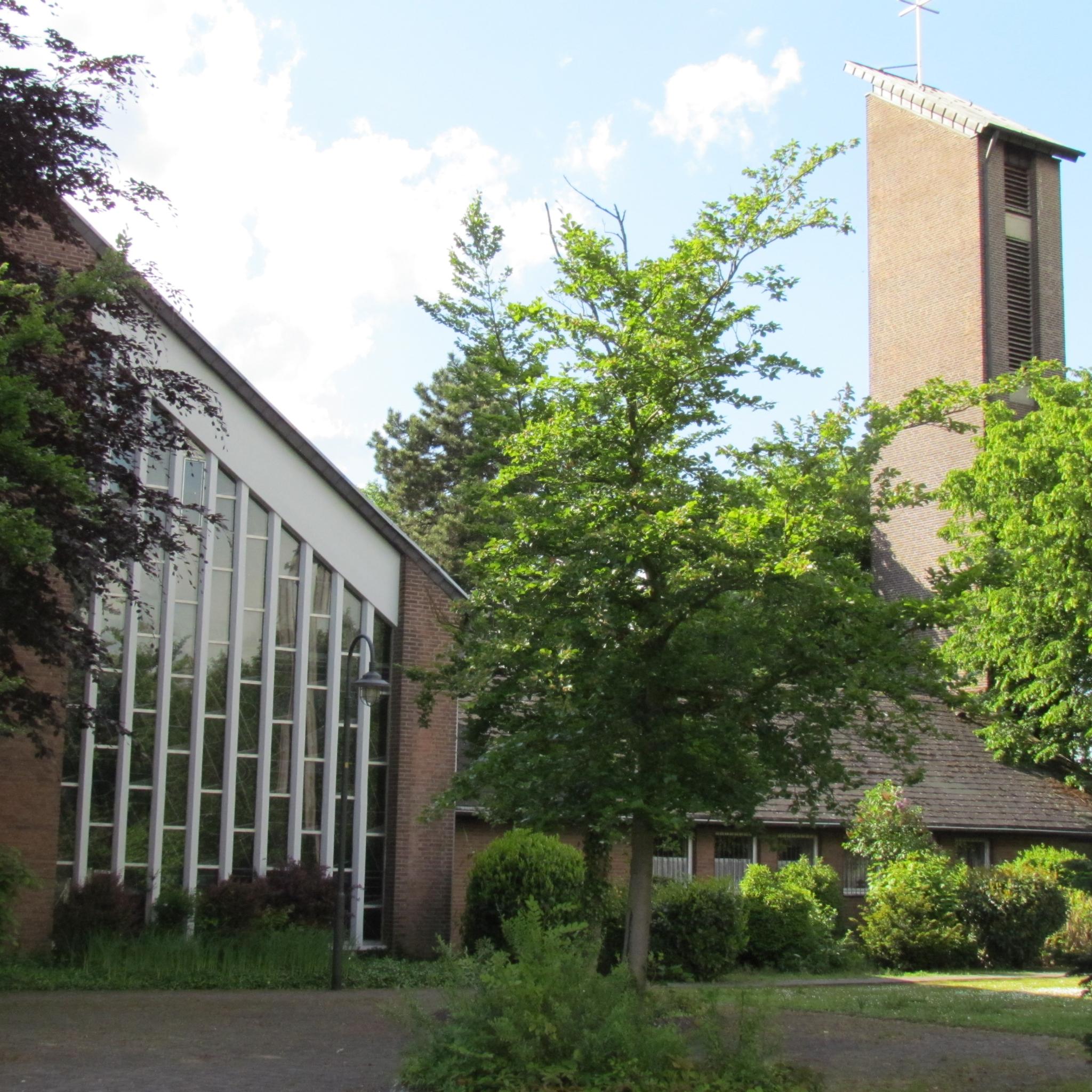zwischen Bäumen scheint das schrägliegende Fenster der Kirche und der daneben stehende Turm mit ebenso schrägem Dach