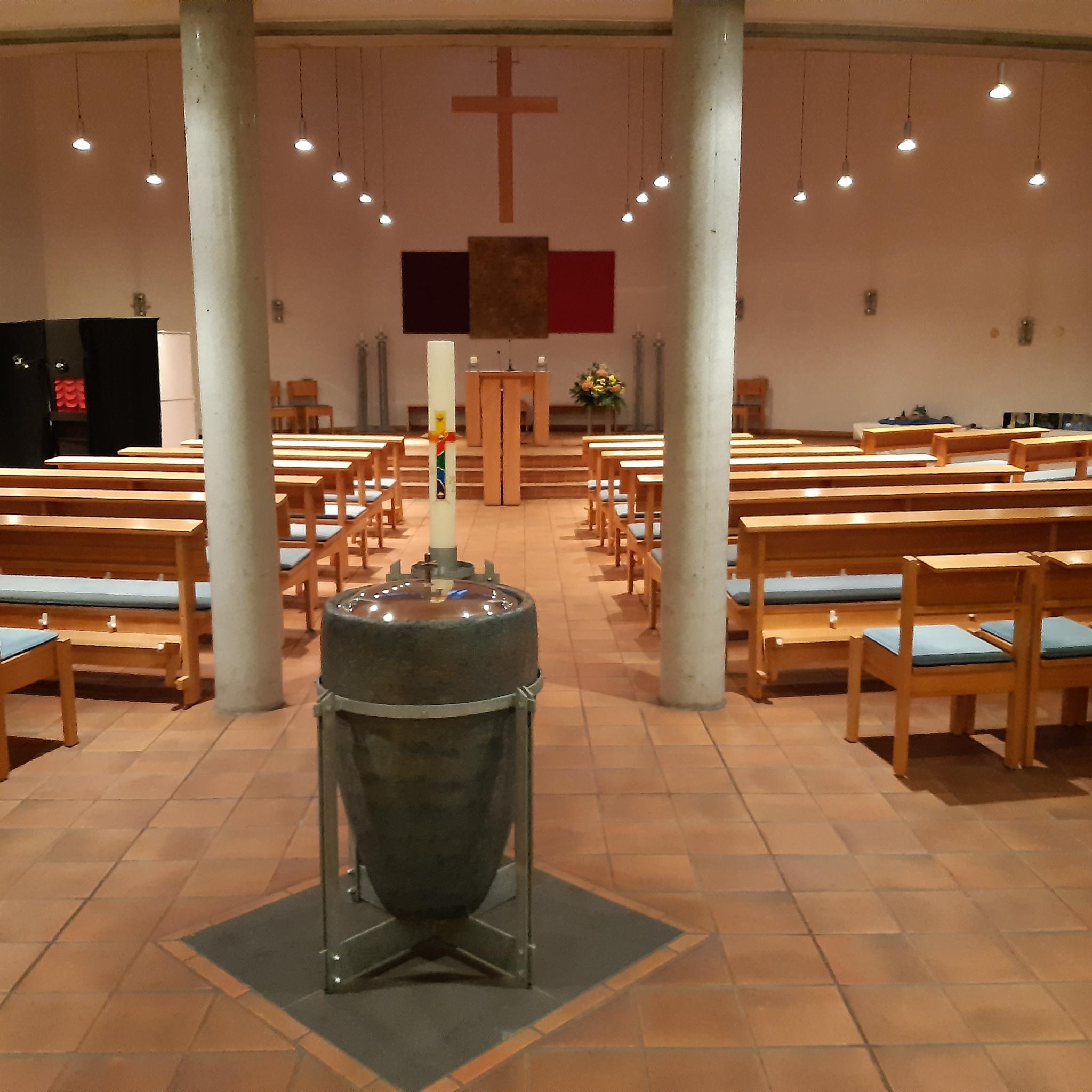Am Taufbecken im Vordergrund führt der Weg Richtung Altar, das ein dreifarbiges neuzeitliches Bild an der Apsiswand ziert