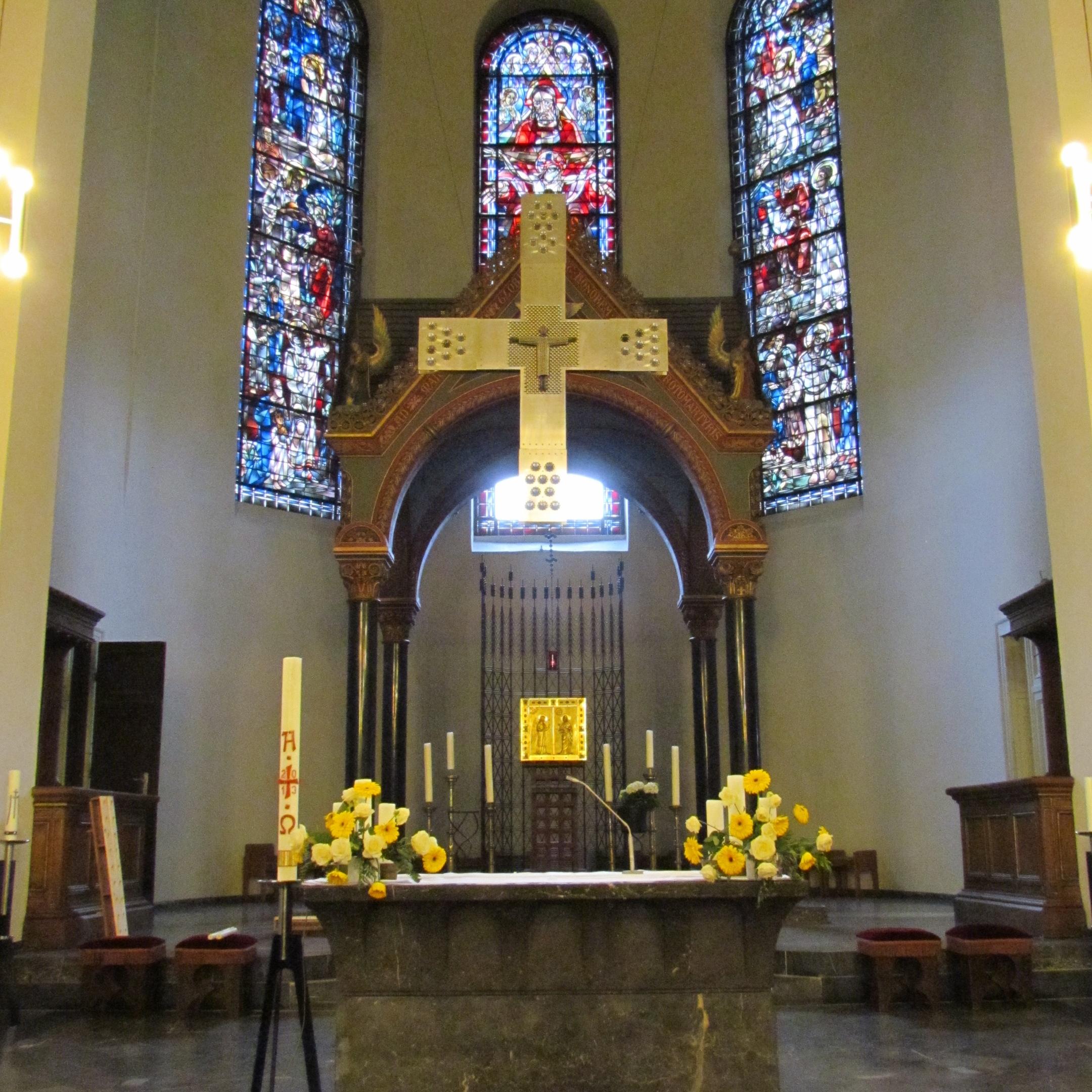 Hinter dem Altar mit Kreuz steht ein steinerner Himmel