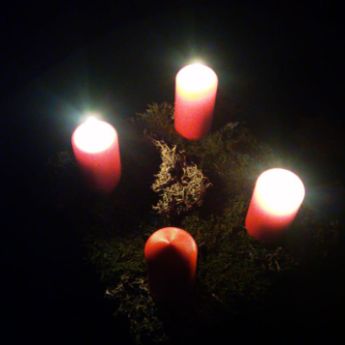 Drei von vier Adventkerzen leuchten in die Dunkelheit