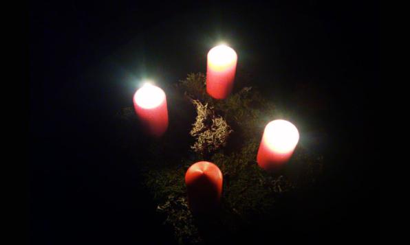 Drei von vier Adventkerzen leuchten in die Dunkelheit