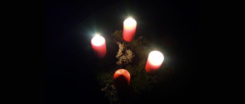 Drei von vier Adventkerzen leuchten in die Dunkelheit