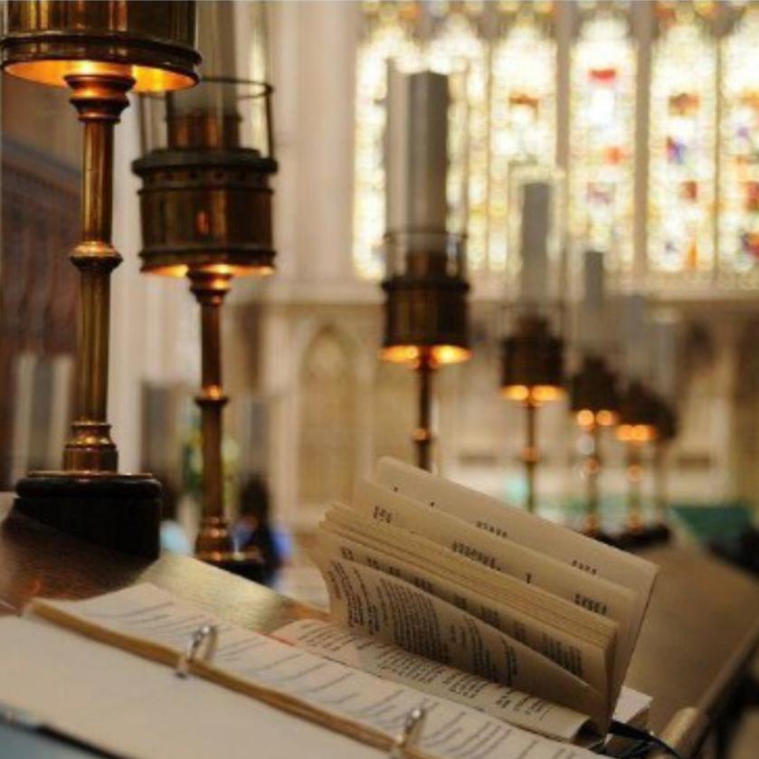 aufgeschlagene Bücher und Mappen liegen auf einer Ablage. Diese ist von Kerzenleuchtern umgeben.