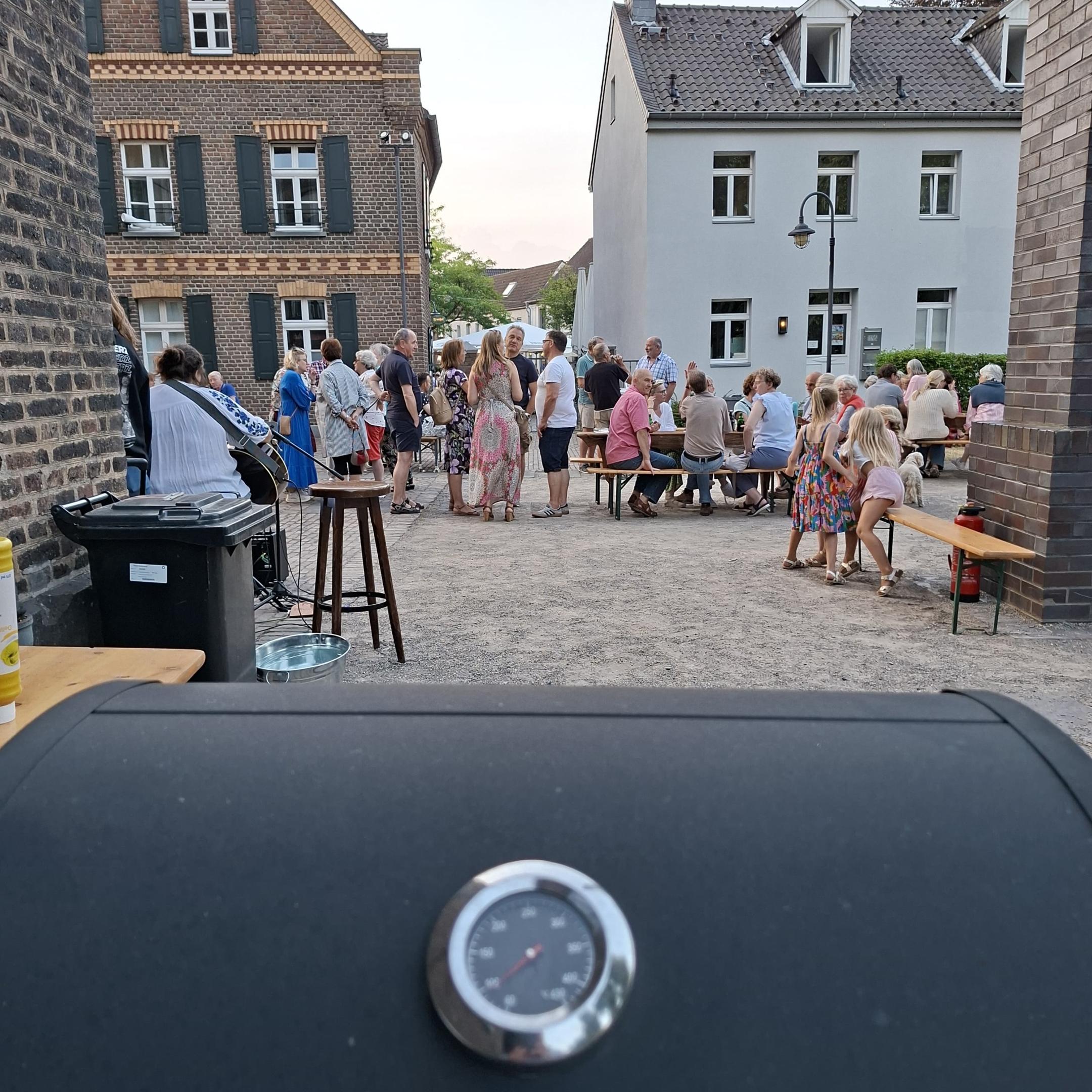 Blick durch die Gasse auf eine Menschenansammlung, dahinter die Häuser der Nachbarschaft der Kirche