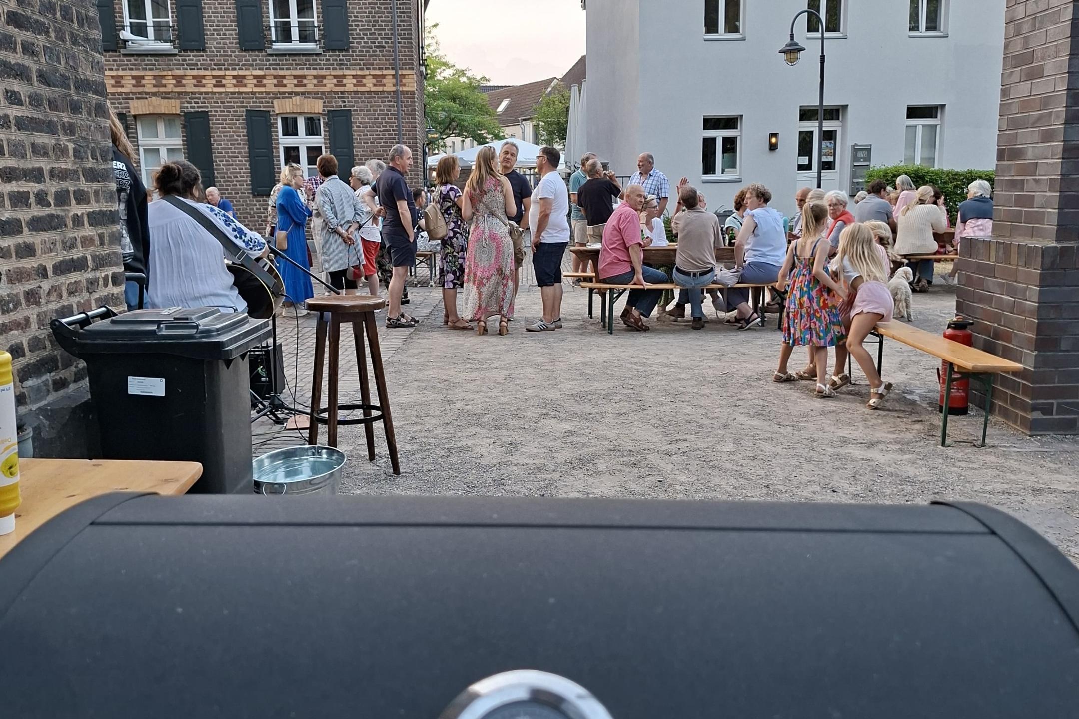 Blick durch die Gasse auf eine Menschenansammlung, dahinter die Häuser der Nachbarschaft der Kirche