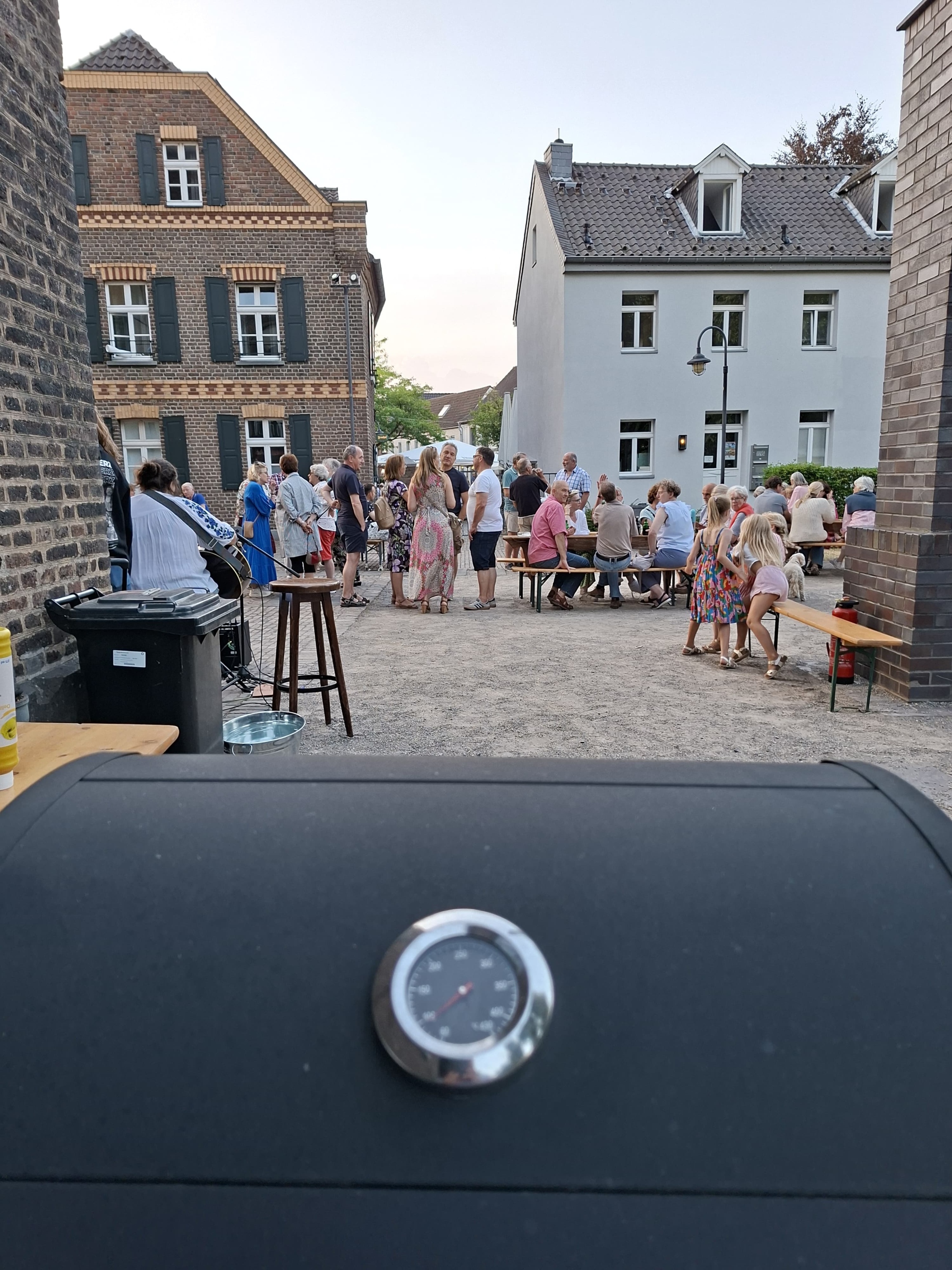 Blick durch die Gasse auf eine Menschenansammlung, dahinter die Häuser der Nachbarschaft der Kirche