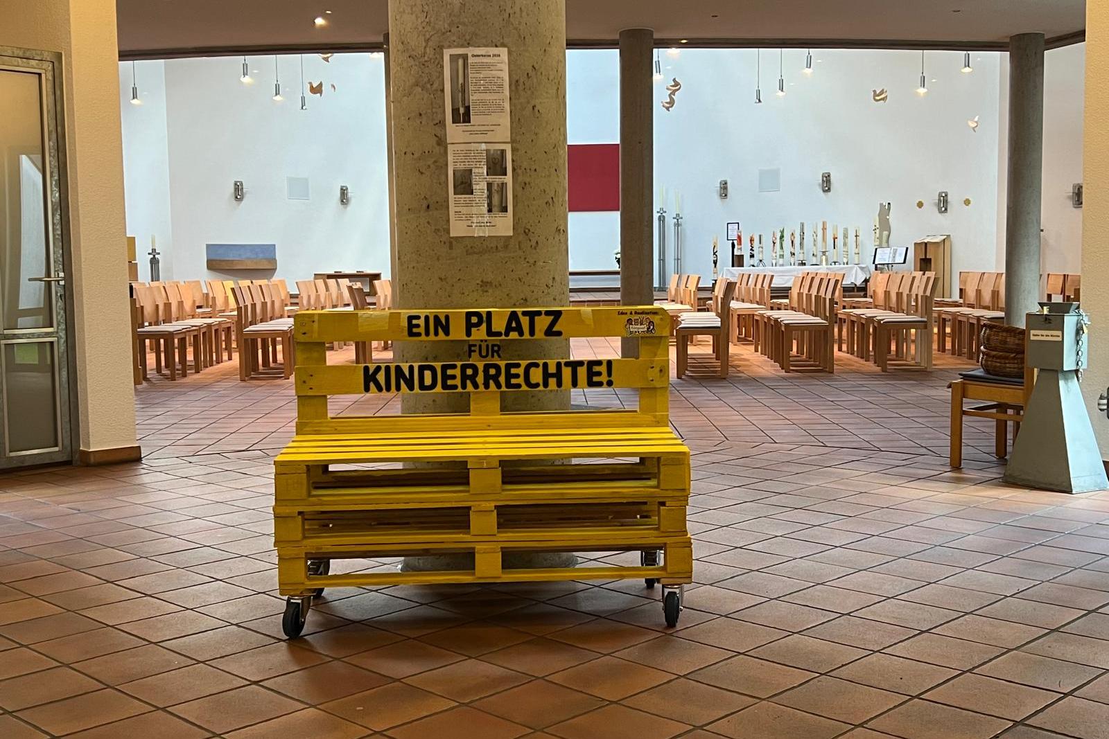 Ein gelbes Palettensofa steht vor einer grauen Säule.
